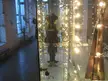 Mirror selfie of a person in a black leather jacket in a room with brick walls, string lights, and a wooden instrument