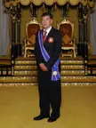 Datuk Ng Joo Ngan in a black suit and blue sash with medals in an ornate room with gold-trimmed thrones.