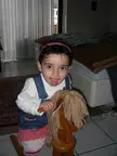 Ayesha wearing a pink headband and denim overalls sitting on a wooden rocking horse