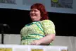 Cassandra Clare, a plus-size redhead with pale skin, wearing a green and white floral print dress.