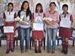 Five Indian girls in school uniforms with red skirts and white shirts holding certificates and flowers in Mizoram