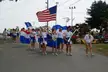 Chivettes in white shirts and blue skirts marching in a parade with American and red and blue flags