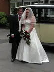Plus-size woman in a white satin wedding dress and a man in a black morning suit by a vintage car
