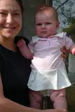 A woman with brown hair and a baby in a pink polo shirt and white tennis skirt.
