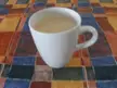 Cursed stock photo of a white ceramic mug with light-colored liquid on a colorful checkered tablecloth.