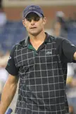Andy Roddick wearing a dark blue Lacoste baseball cap and a black grid-patterned athletic polo shirt.